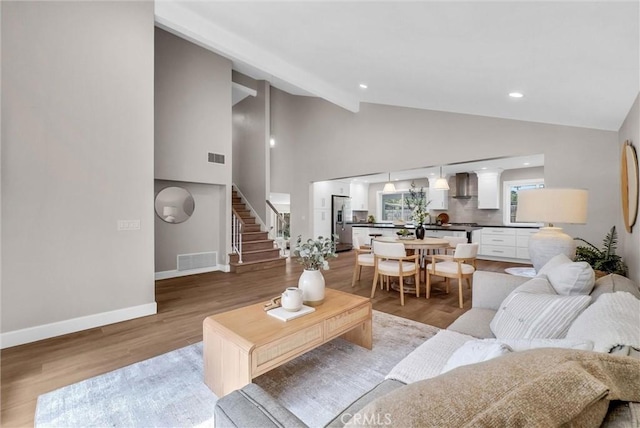 living room with stairs, vaulted ceiling, visible vents, and light wood-type flooring