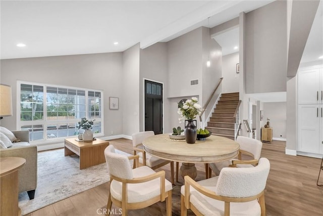 dining space featuring high vaulted ceiling, light wood-type flooring, stairs, and visible vents