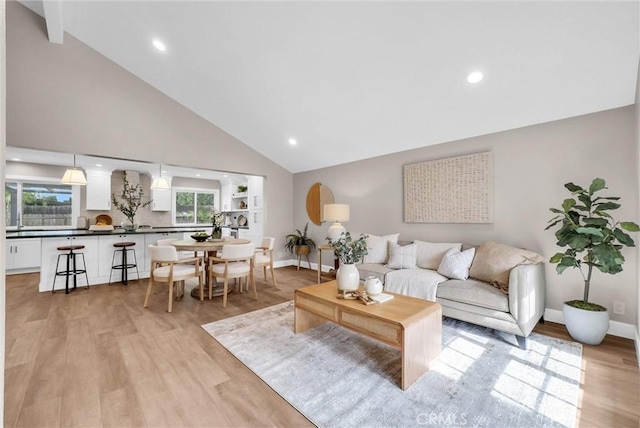 living area with light wood-style floors, baseboards, a healthy amount of sunlight, and high vaulted ceiling