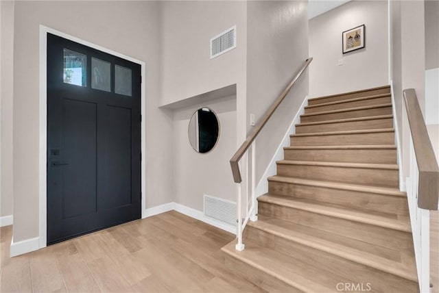 foyer entrance with visible vents, baseboards, wood finished floors, and stairway