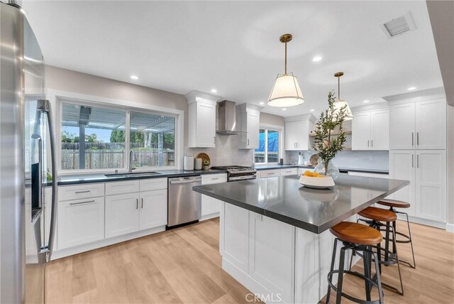 kitchen with wall chimney range hood, a sink, stainless steel appliances, white cabinetry, and visible vents