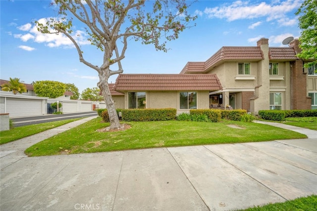 view of front of house featuring a tiled roof, a chimney, a front lawn, and stucco siding