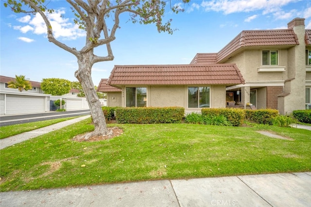view of front of property featuring a front lawn, stucco siding, mansard roof, and a tile roof