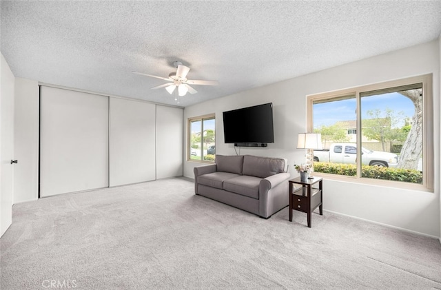 carpeted living area with baseboards, a textured ceiling, and ceiling fan