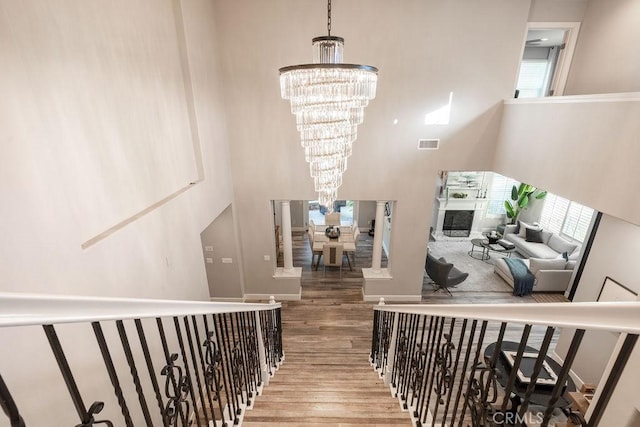 stairway featuring an inviting chandelier, wood finished floors, visible vents, and a towering ceiling