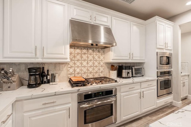 kitchen featuring decorative backsplash, white cabinetry, appliances with stainless steel finishes, and under cabinet range hood