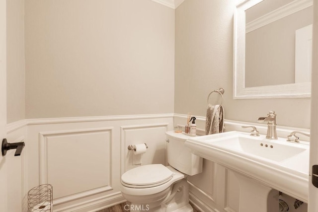 half bath featuring wainscoting, crown molding, a decorative wall, and toilet