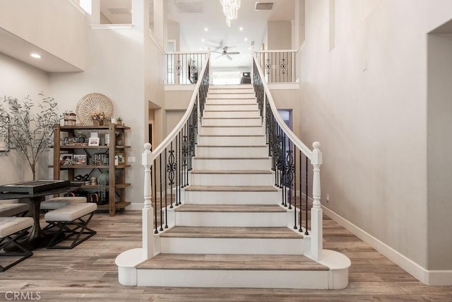 stairs featuring baseboards, a high ceiling, wood finished floors, and ceiling fan with notable chandelier