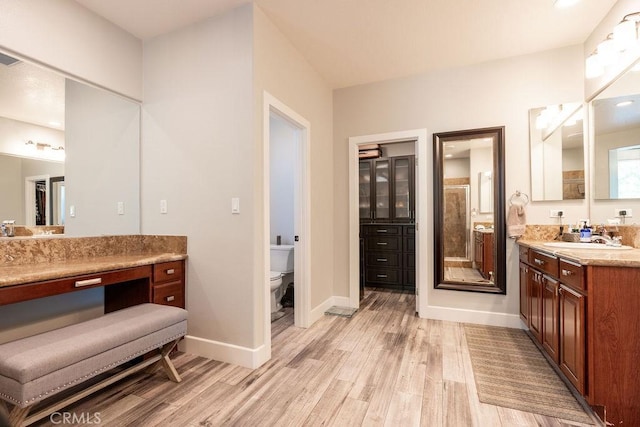 bathroom featuring vanity, wood finished floors, toilet, baseboards, and a shower stall