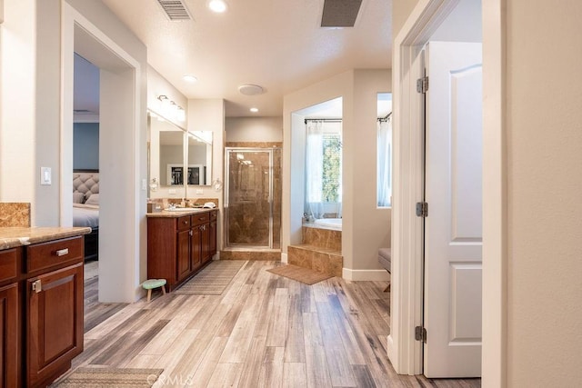 ensuite bathroom with vanity, a shower stall, wood finished floors, and visible vents