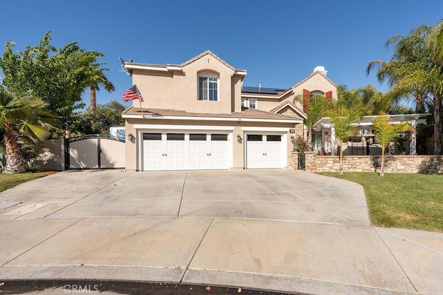 traditional-style house featuring driveway, solar panels, a gate, an attached garage, and stucco siding