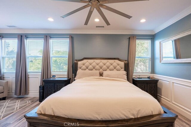 bedroom featuring visible vents, wainscoting, wood finished floors, a decorative wall, and a ceiling fan
