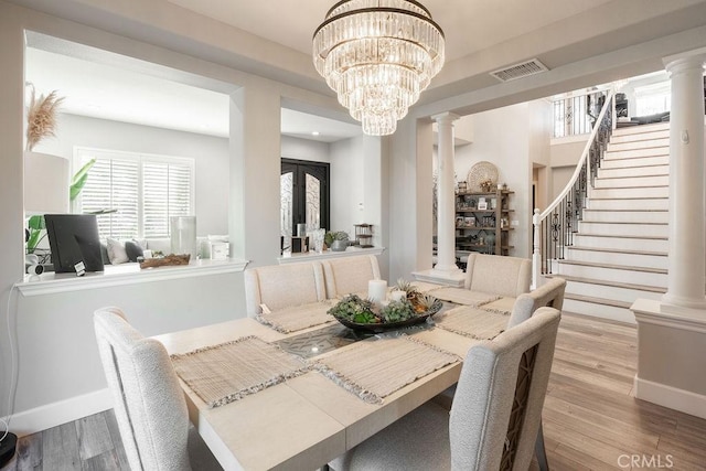 dining room featuring visible vents, decorative columns, wood finished floors, stairway, and a notable chandelier