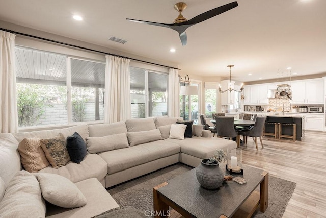living area with visible vents, recessed lighting, light wood-style floors, and ceiling fan with notable chandelier