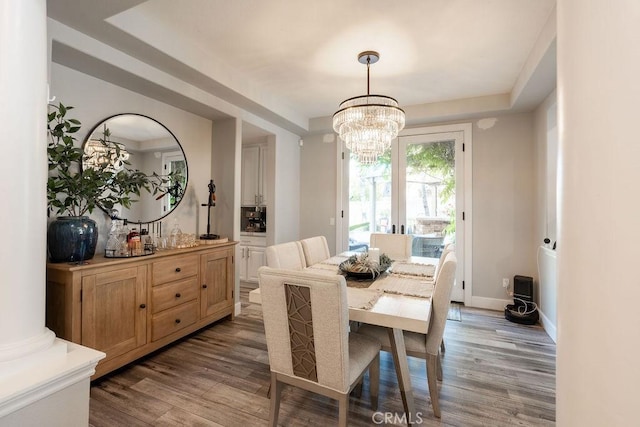 dining area with a raised ceiling, baseboards, wood finished floors, and a chandelier