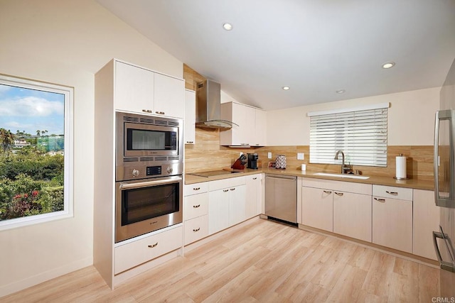 kitchen with stainless steel appliances, decorative backsplash, a sink, and wall chimney exhaust hood