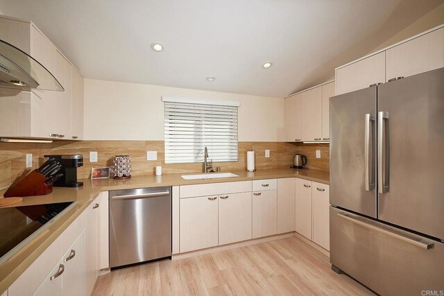 kitchen with decorative backsplash, light countertops, a sink, light wood-style flooring, and appliances with stainless steel finishes