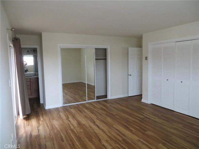 unfurnished bedroom with baseboards, two closets, and wood finished floors