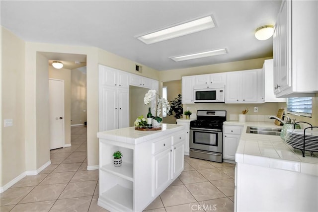 kitchen with white microwave, tile countertops, stainless steel range with gas stovetop, a sink, and light tile patterned floors