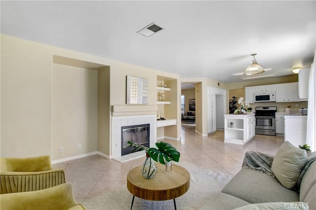 living area featuring light tile patterned flooring, built in shelves, a tiled fireplace, baseboards, and visible vents
