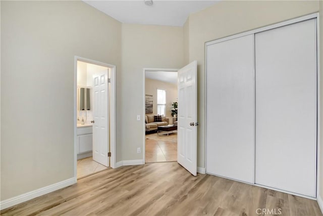 unfurnished bedroom with light wood-style floors, baseboards, ensuite bath, and a closet