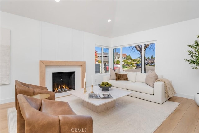 living room featuring recessed lighting, baseboards, light wood finished floors, and a warm lit fireplace