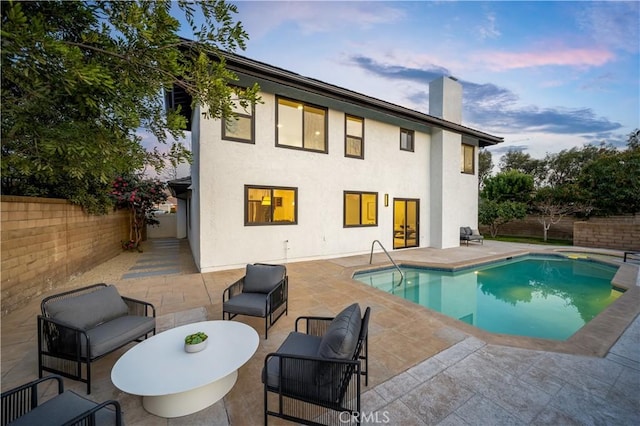 rear view of property with a fenced in pool, a fenced backyard, a patio area, and a chimney