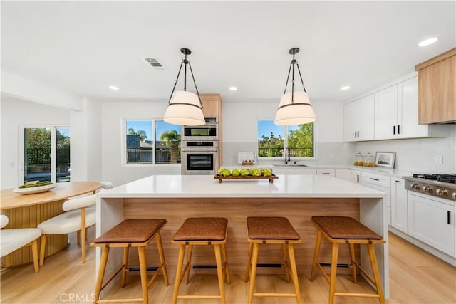 kitchen with a sink, stainless steel gas stovetop, light wood finished floors, and a kitchen bar