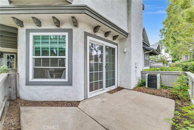 view of exterior entry featuring central air condition unit, stucco siding, and a patio area