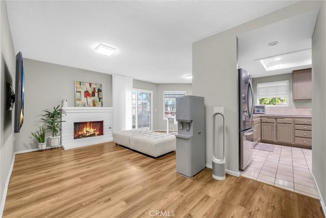 living room featuring baseboards, light wood-style flooring, a brick fireplace, and a wealth of natural light