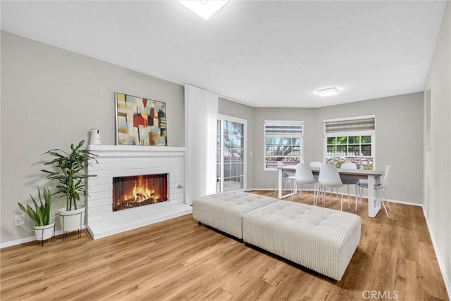 living room featuring a brick fireplace, baseboards, and wood finished floors