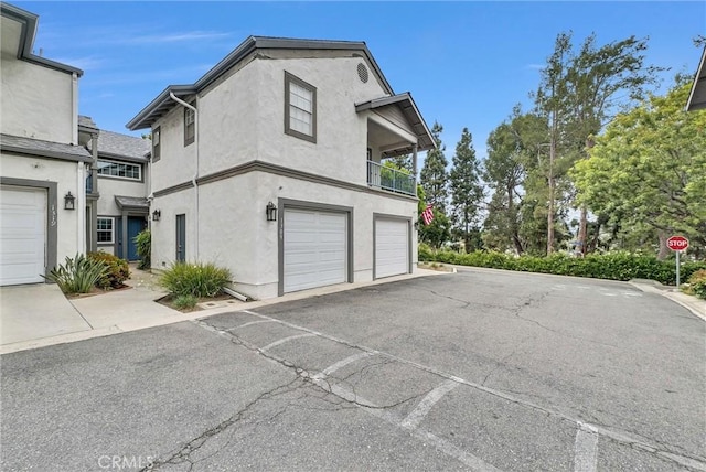 view of side of home with an attached garage, stucco siding, a balcony, and driveway