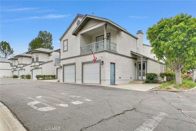 view of front facade featuring an attached garage, stucco siding, a chimney, a balcony, and driveway
