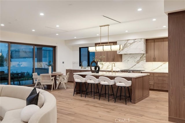 932 9th St, Manhattan Beach, CA 90266 - kitchen featuring wall chimney range hood, light wood-type flooring, a center island with sink, light countertops, and backsplash