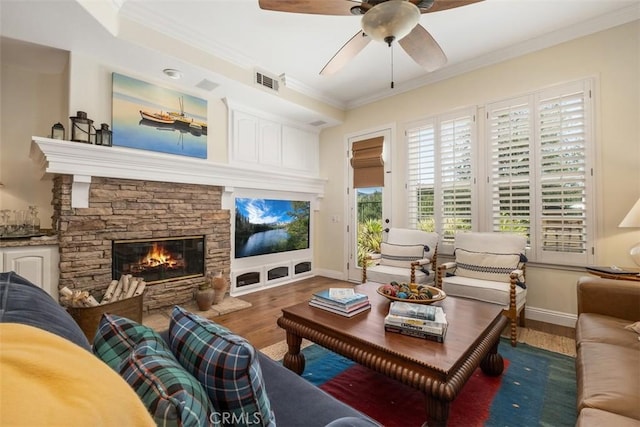living area featuring crown molding, visible vents, wood finished floors, a stone fireplace, and ceiling fan