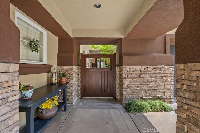 doorway to property with a gate, stucco siding, and stone siding