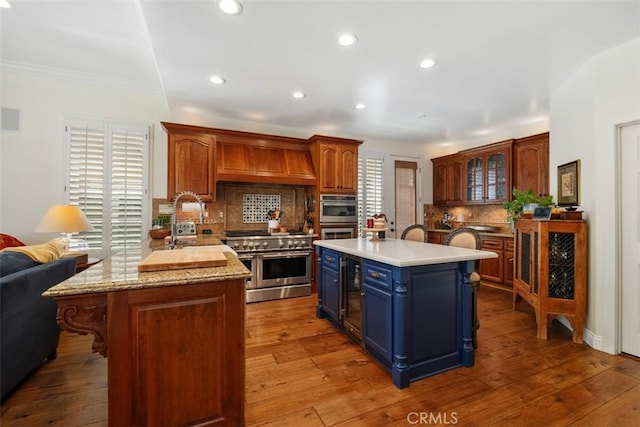 kitchen with crown molding, appliances with stainless steel finishes, backsplash, custom exhaust hood, and blue cabinets