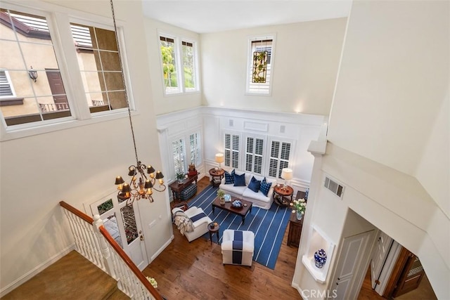 living area with visible vents, an inviting chandelier, a decorative wall, wood finished floors, and a wainscoted wall