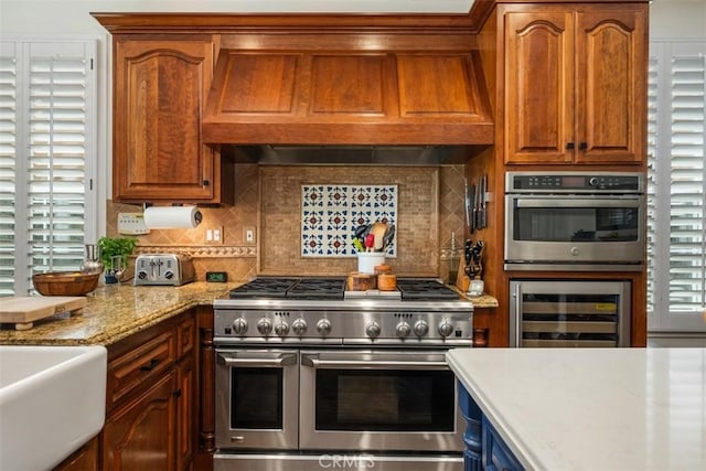 kitchen with light stone counters, beverage cooler, stainless steel appliances, tasteful backsplash, and custom exhaust hood