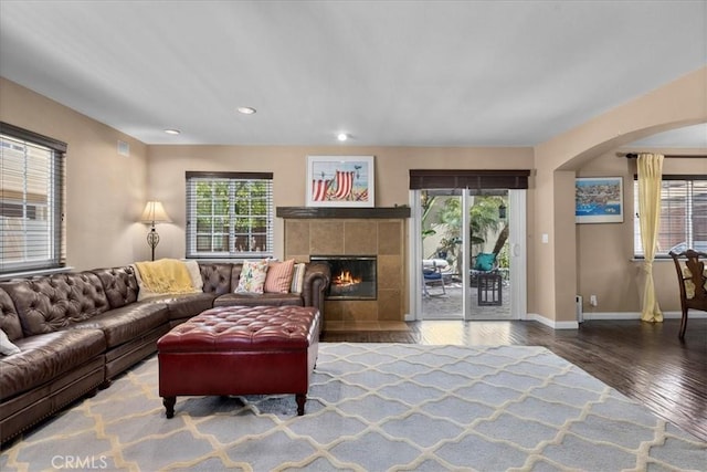 living area featuring a tiled fireplace, arched walkways, wood finished floors, baseboards, and recessed lighting