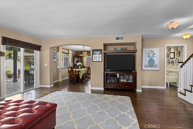 living area with a notable chandelier, arched walkways, stairs, wood finished floors, and visible vents
