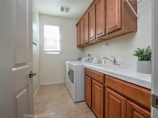 washroom with visible vents, cabinet space, a sink, baseboards, and washer and clothes dryer