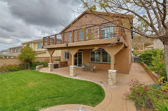 rear view of house featuring fence, stucco siding, a patio area, a balcony, and a lawn