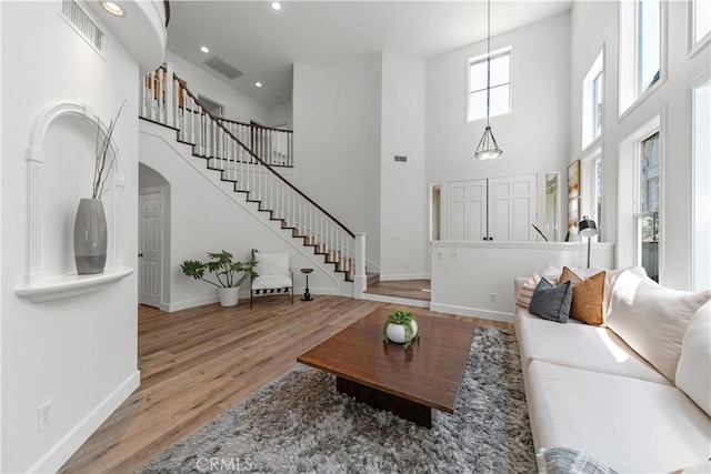 living area featuring visible vents, stairs, wood finished floors, baseboards, and a high ceiling