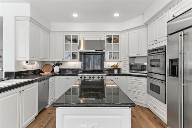 kitchen with appliances with stainless steel finishes, white cabinetry, a sink, under cabinet range hood, and light wood-style flooring