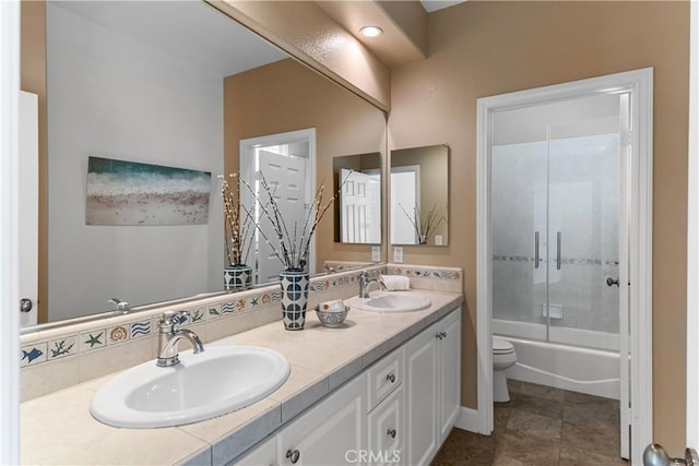 full bathroom featuring double vanity, a sink, shower / bath combination with glass door, and toilet