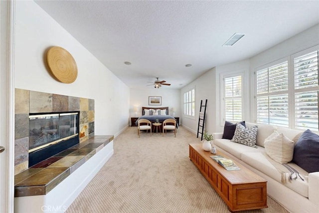 living area with light carpet, a ceiling fan, baseboards, a tile fireplace, and visible vents