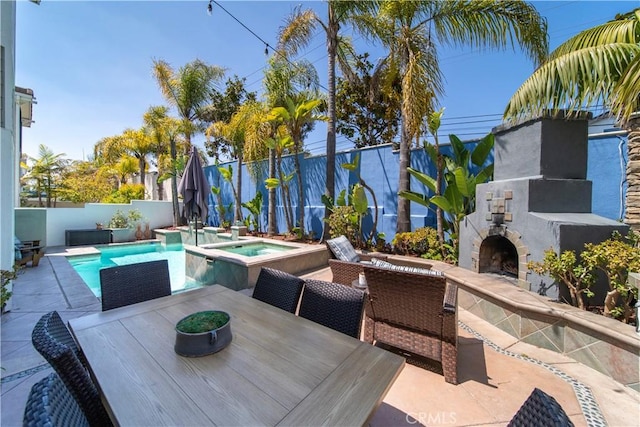 view of patio / terrace featuring an in ground hot tub, an outdoor stone fireplace, a fenced in pool, a fenced backyard, and outdoor dining space
