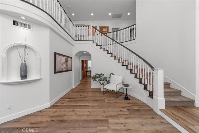 entrance foyer featuring stairs, arched walkways, visible vents, and wood finished floors