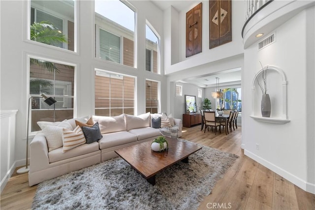 living room featuring light wood-style floors, baseboards, a towering ceiling, and visible vents